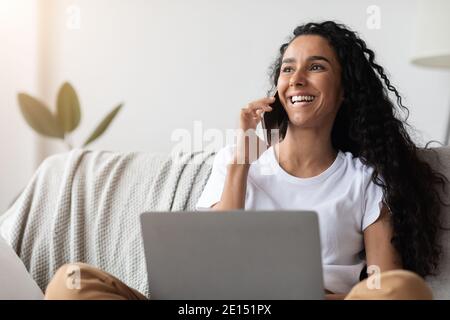 Cheerful woman freelancer talking on phone and using laptop Stock Photo