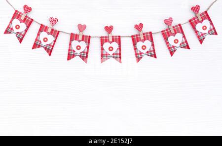 Banner with red checkered flags and wooden hearts on a thread isolated on white background. Flags on a jute rope dedicated to Valentine's day for gree Stock Photo