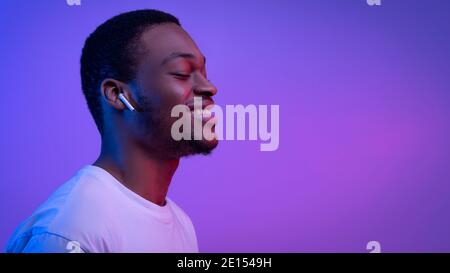 Relaxed African Man Listening Music In Wireless Airpods Earphones In Neon Light Stock Photo