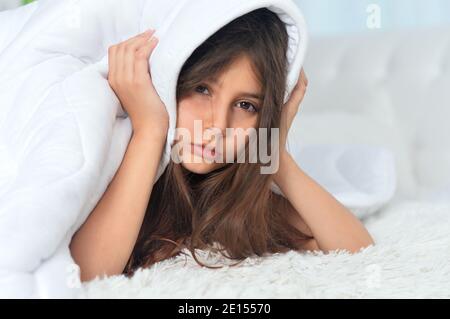 Cute little girl covering head trying to sleep in noisy room Stock Photo