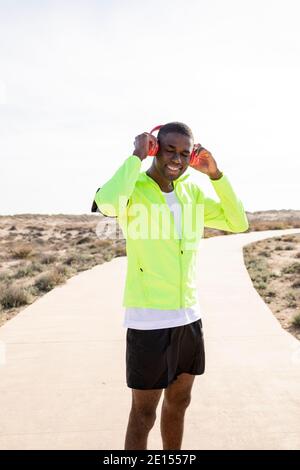 Vertical shot of a Young smiling black runner in a yellow rain jacket who enjoys listening to music on his cell phone before or after training. Stock Photo