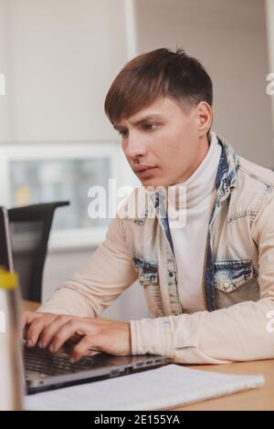 Vertical close up of a young man looking focused, typing on his laptop Stock Photo