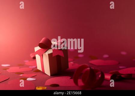 Paper art Valentine's day concept banner with hand made gift box, paper cut ribbon, bow, and a lot of hearts on red background with space for text. Stock Photo