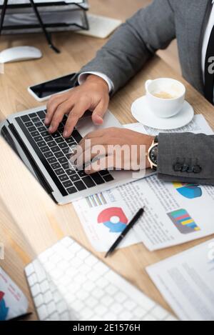 partial view of trader typing on laptop near coffee cup and papers with infographics Stock Photo