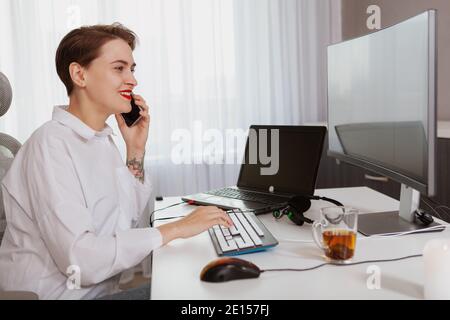 Lovely young businesswoman talking on her smart phone while working on a computer Stock Photo