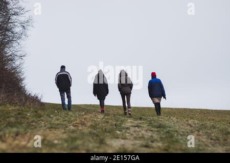 A group of people walk side by side through the countryside in cold weather, back view Stock Photo