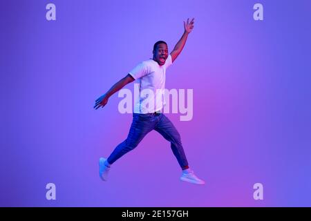 Excited Funny Black Guy Jumping Up In Neon Light Over Purple Background Stock Photo
