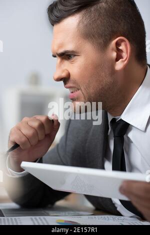 worried trader holding pen in office, blurred foreground Stock Photo