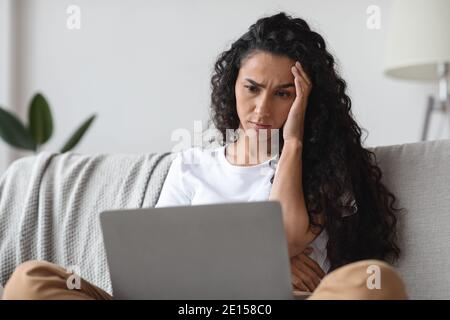 Troubled young woman sitting on couch with laptop, closeup Stock Photo