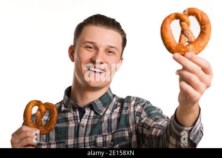 Happy young handsome man smiling joyfully holding delicious pretzels in his hands isolated on white. Attractive cheerful man holding out tasty snack p Stock Photo