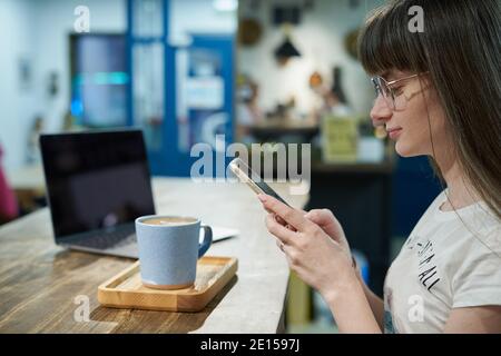 Young woman takes photos using smartphone of his coffee in mug for blogging Stock Photo