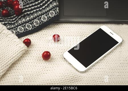 Composition with knitted background, sweaters, decoration and black smartphone, copy space, cozy photo Stock Photo