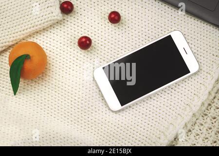 Winter cozy composition, tangerines, decoration and smartphone on blachround of kniteed warm sweaters, copy space photo Stock Photo