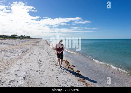 Man looks out at the ocean as he walks down beach with hands behind back Stock Photo