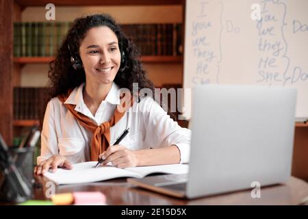 Student sitting at table, using laptop and writing in notebook Stock Photo