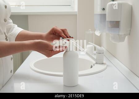 Cropped view of female hands pressing on soap bottle before washing hands in a sink Stock Photo