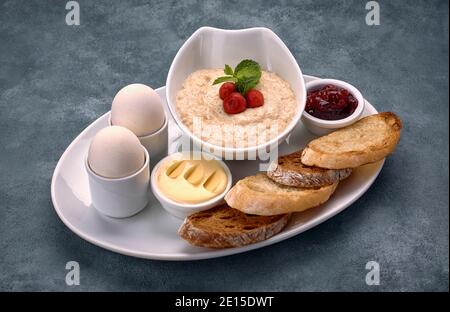 Breakfast of porridge, butter, boiled eggs, jam and toast, croutons, on a gray-blue background Stock Photo