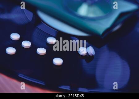 selective focus photo of pills on vinyl record background, surrounded by bright club illumination Stock Photo
