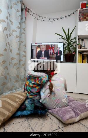 Chichester, West Sussex, UK. Florence, 5, (left) and her sister Isabelle, 8, (right) watching the UK Prime Minister Boris Johnson giving his speech at 8pm on Monday 4th January 2021 putting the UK in it's 3rd Lockdown and closing schools. Credit: Sam Stephenson/Alamy Live News Stock Photo