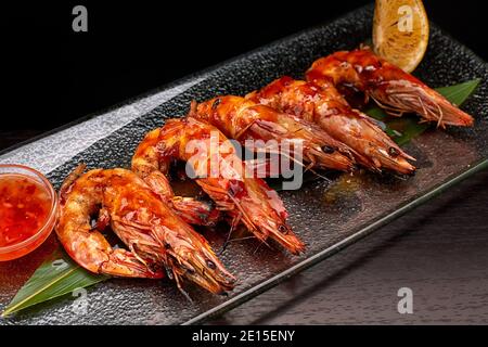 Fried king prawns on a bamboo leaf, on a transparent plate, with lemon and sauce Stock Photo