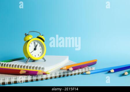Mechanical alarm clock, notebook, pencils on the blue background Stock Photo