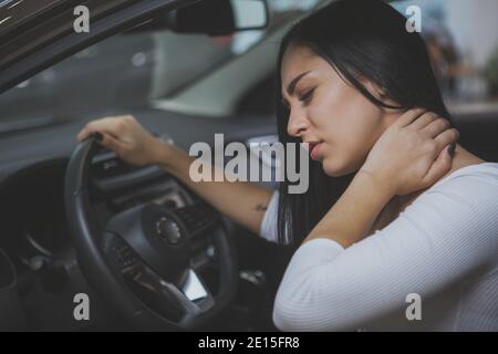 Beautiful young woman rubbing her neck, feeling sore after long drive. Female driver having terrible neck pain after whiplash injury in car crash. Hea Stock Photo