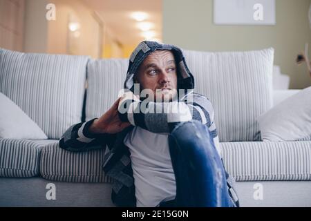 A handsome man sits on the floor in the living room and thinks how to solve a problem. Stock Photo