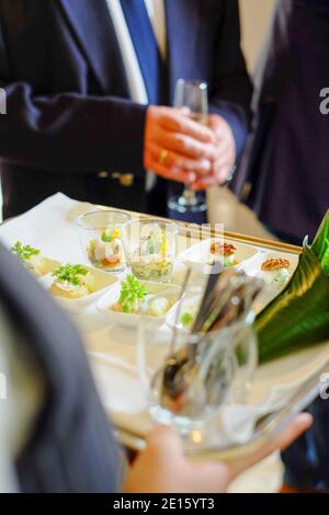 Waiter holding a tray of appetizers at a reception, guests in suits with champagne Stock Photo
