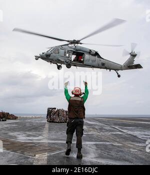 Indian Ocean, United States. 04th Jan, 2021. U.S. Navy Airman Daniel Williams, signals an MH-60S Sea Hawk helicopter that they are clear during a vertical replenishment at sea on the flight deck of the Nimitz-class aircraft carrier USS Nimitz January 4, 2021 in the Indian Ocean. The Nimitz was due to return to home port but has been kept in place near Iran due to increased tensions. Credit: Planetpix/Alamy Live News Stock Photo