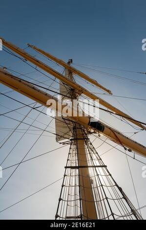 View looking up wooden mast with ropes and rigging from an old sailing ship against a blue sky Stock Photo