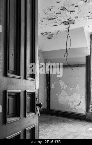 Old wooden door partially open looking into an abandoned empty room. Black and white in vertical orientation. Stock Photo