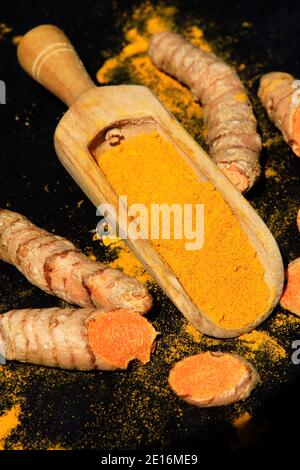Turmeric powder (Kurkuma) in a wooden spoon and roots on a dark table (curcuma longa) Stock Photo