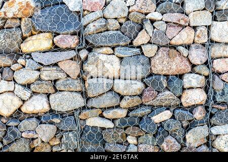 Stone wall with metal grid as background. Rock texture in metal grid. Gabion net Stock Photo