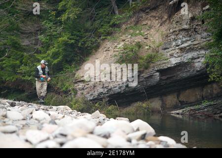 Full length portrait of mature fisherman using rod fly fishing in mountain river. Concept of relaxation during favorite outdoor hobby. Stock Photo