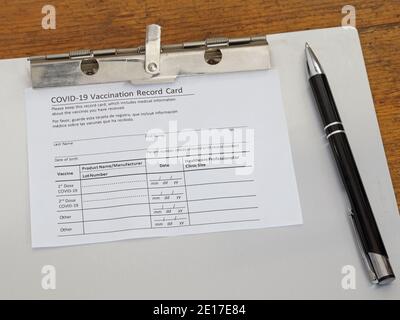 A Coronavirus Covid-19 vaccination record card is shown on an aluminum clipboard in 2021. Stock Photo