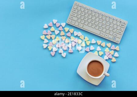 A cup of coffee, candies in a shape of hearts and keyboard on blue table. Top view, flat lay, copy space. Stock Photo