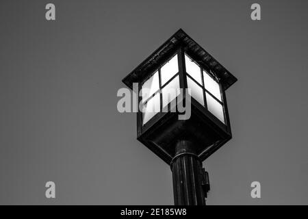Old fashioned lamp post illuminated against the night sky. Black and white in horizontal orientation with copy space. Stock Photo