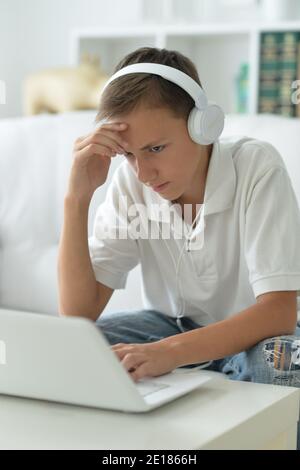 Sad boy in headphones using laptop in room Stock Photo