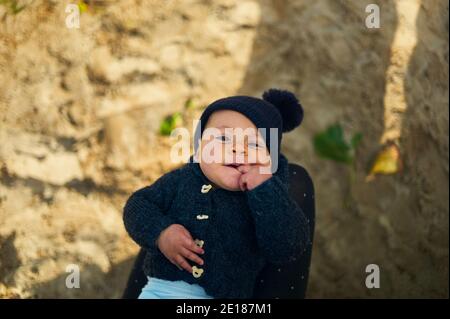 A little baby is resting in his mothers lap on a sunny autumn day in the park Stock Photo