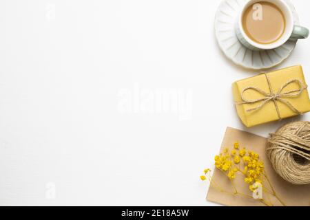 Anniversary concept. Yellow gift box, cup of coffee, card with dry flowers on white background. flat lay, top view, copy space Stock Photo