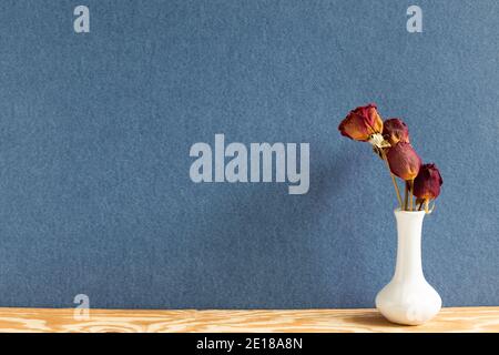 Vase of dry red rose on wooden table. blue background. flower arrangement Stock Photo