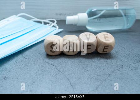 SAVE and SAFE word written on wood block with Medical protective mask and hand sanitizer gel. Hand hygiene corona virus protection. against infection. Stock Photo