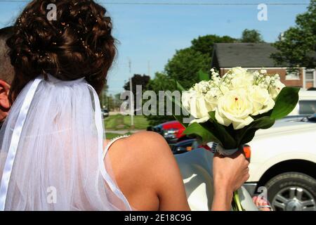 A brunette bride with birdseed in her hair lifts her white rose bouquet as she is carried by her new husband. Stock Photo