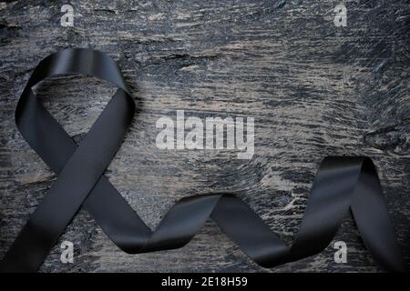 Top view of black ribbon on dark wood background with copy space. Melanoma or skin cancer, gang prevention and narcolepsy awareness concept. Stock Photo