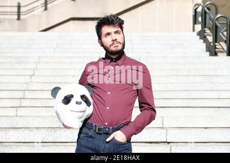 Young business man with a panda head mask in his hands, standing on stairs. Bizarre businessman. Stock Photo