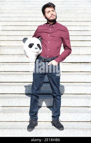 Young business man with a panda head mask in his hands, standing on stairs. Bizarre businessman. Stock Photo