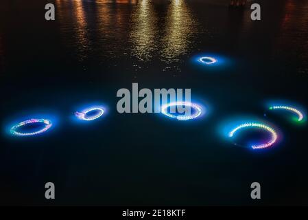 Underwater neon or led multi coloured lights rings (circles) shine on the dark sea bottom or seafloor representing organisms glowing in darkness Stock Photo