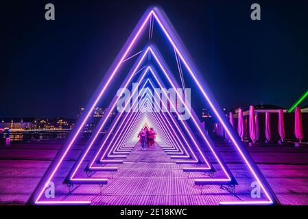 Purple coloured gate of light or light tunnel installation made of triangular neon and led lights. Blurred people walk through the bright deep passage Stock Photo