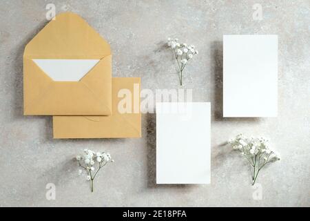 Wedding stationery set on stone table top view. Flat lay blank invitation cards, envelopes, flowers. Stock Photo