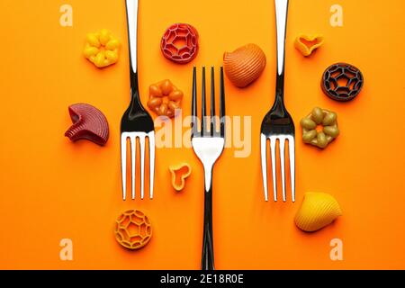 three forks with some types of colored pasta on an orange surface Stock Photo